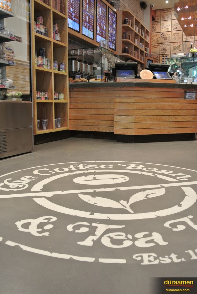 The warm grays in this Skraffino applied concrete resurfacing showcase the logo of this popular NYC coffee shop.