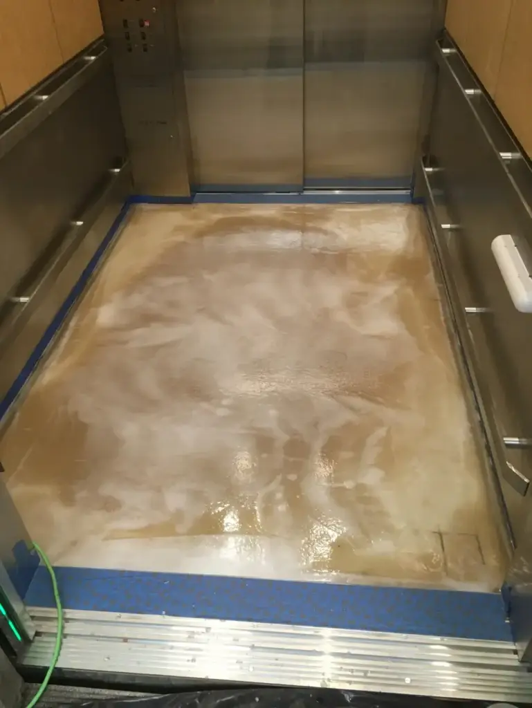 Spiderlath fiberglass reinforcement embedded in Perdure MVT+ moisture vapor barrier during freight elevator floor coating installation