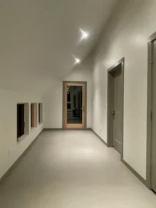 Long hallway with continuous Arapido microcement flooring and recessed lighting.